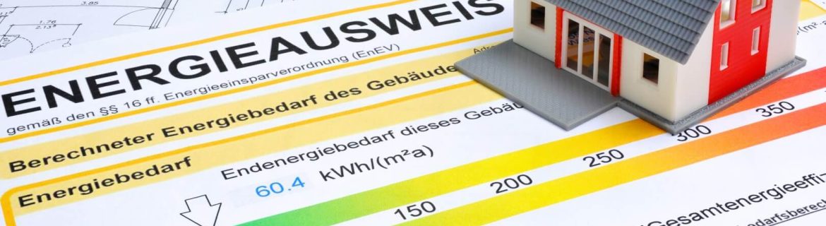 Ein Modellhaus steht auf einem Energieausweis mit Farbskala und detaillierten Energieeffizienzklassen, darüber sind Baupläne sichtbar.