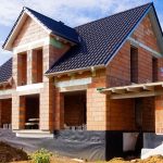 Ein Einfamilienhaus im Rohbau mit Ziegeldach. Die Außenwände sind aus roten Ziegelsteinen errichtet, und die Fenster- und Türöffnungen sind sichtbar.