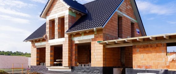 Ein Einfamilienhaus im Rohbau mit Ziegeldach. Die Außenwände sind aus roten Ziegelsteinen errichtet, und die Fenster- und Türöffnungen sind sichtbar.