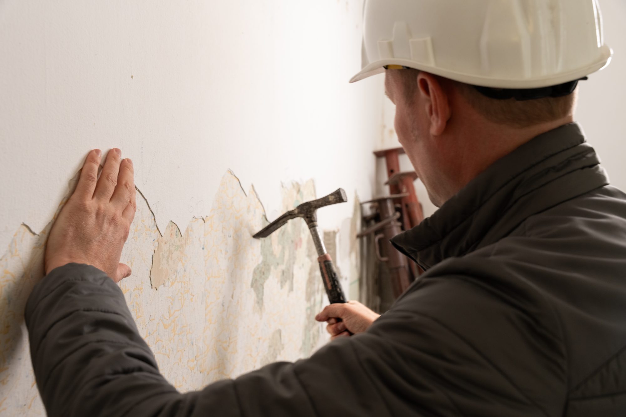 Baumeister Franz Grassl legt die Hand an eine Wand mit abplatzendem Putz und prüft sie mit dem Hammer