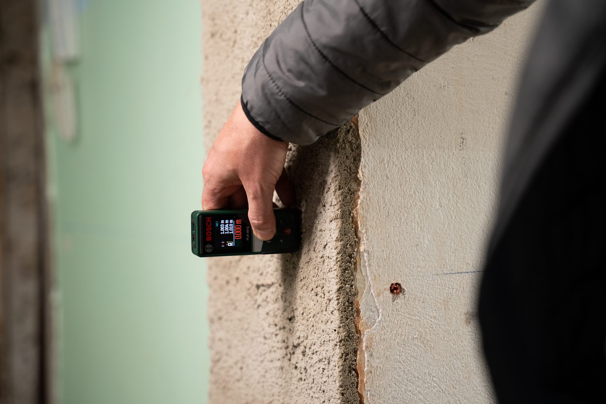 Eine Hand hält auf der Baustelle ein Messgerät mit Display an eine Türleibung