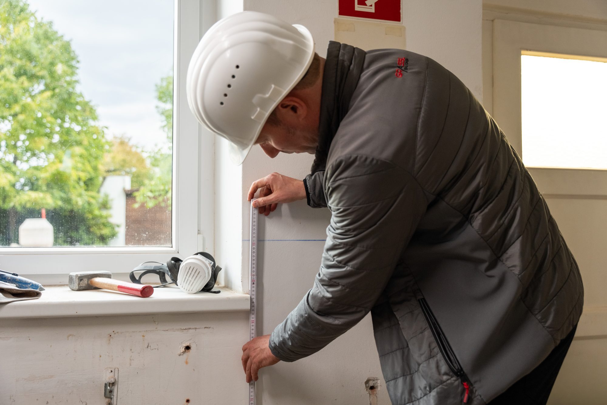 Baumeister Franz Grassl mit Bauhelm prüft in einem Bestandsgebäude die Laibung eines Fensters